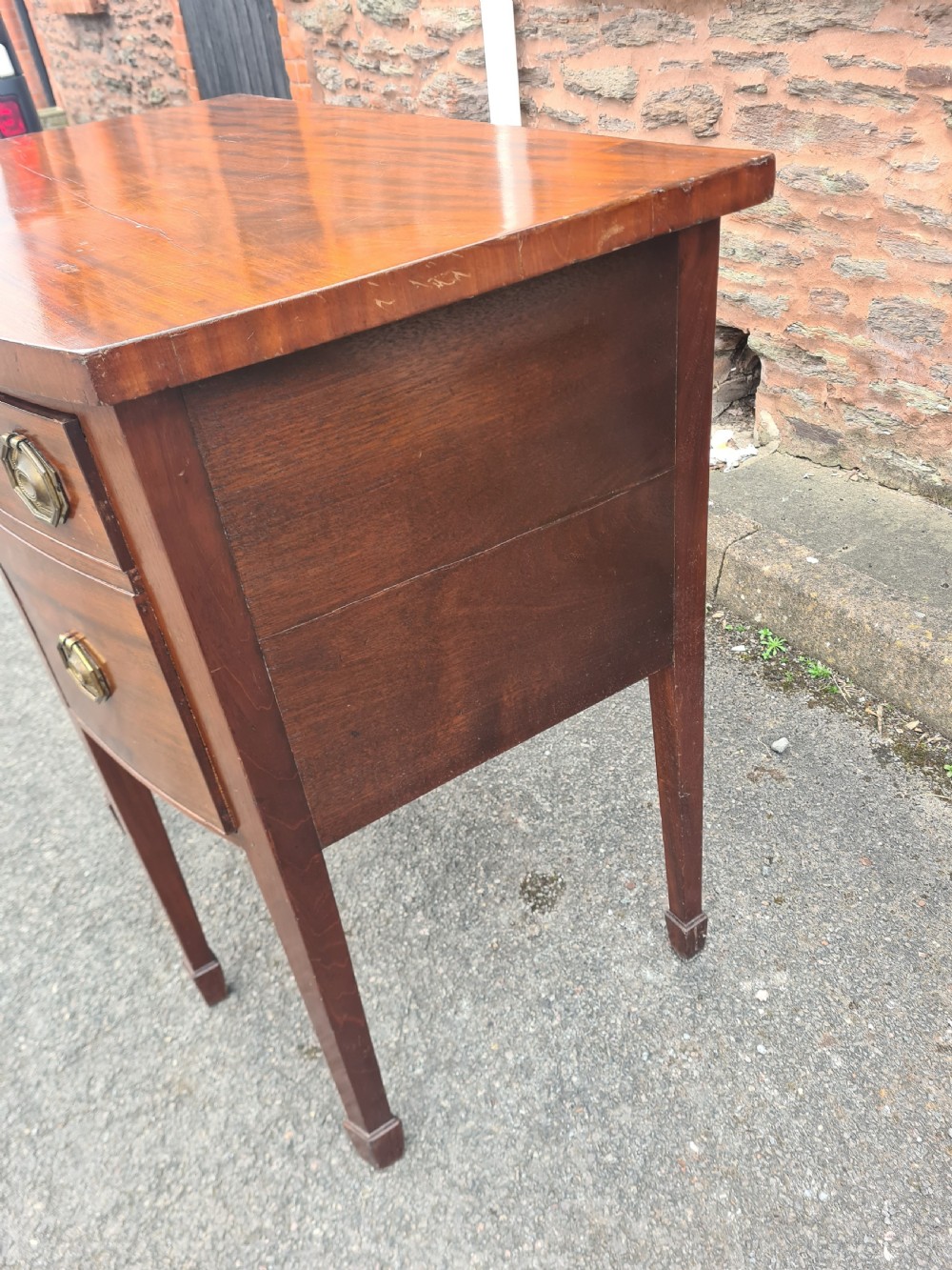 A Georgian mahogany bowfront sideboard featuring a curved front, octagonal brass handles, three drawers, and four square tapered legs. View II
