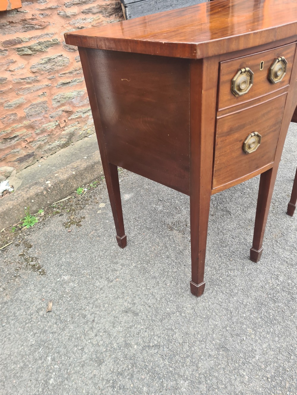 A Georgian mahogany bowfront sideboard featuring a curved front, octagonal brass handles, three drawers, and four square tapered legs. View V