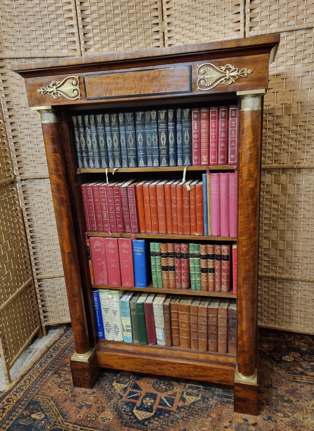 A French Empire open mahogany bookcase featuring carved fluted side columns with brass capitals, upper ormolu mounts, and four open shelves filled with books.