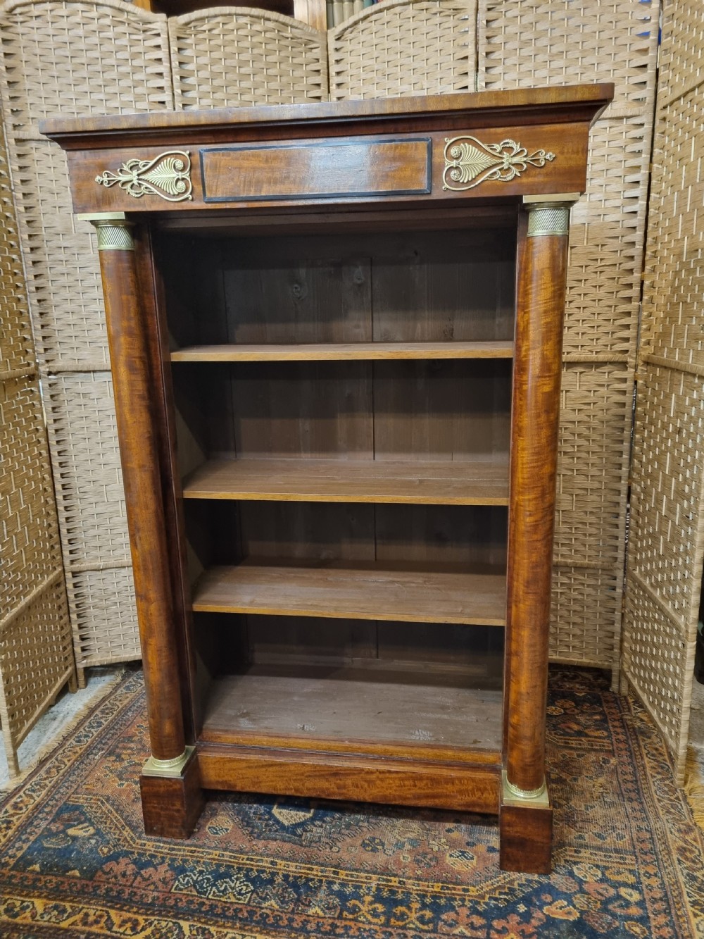 A French Empire open mahogany bookcase featuring carved fluted side columns with brass capitals, upper ormolu mounts, and four open shelves filled with books. View II