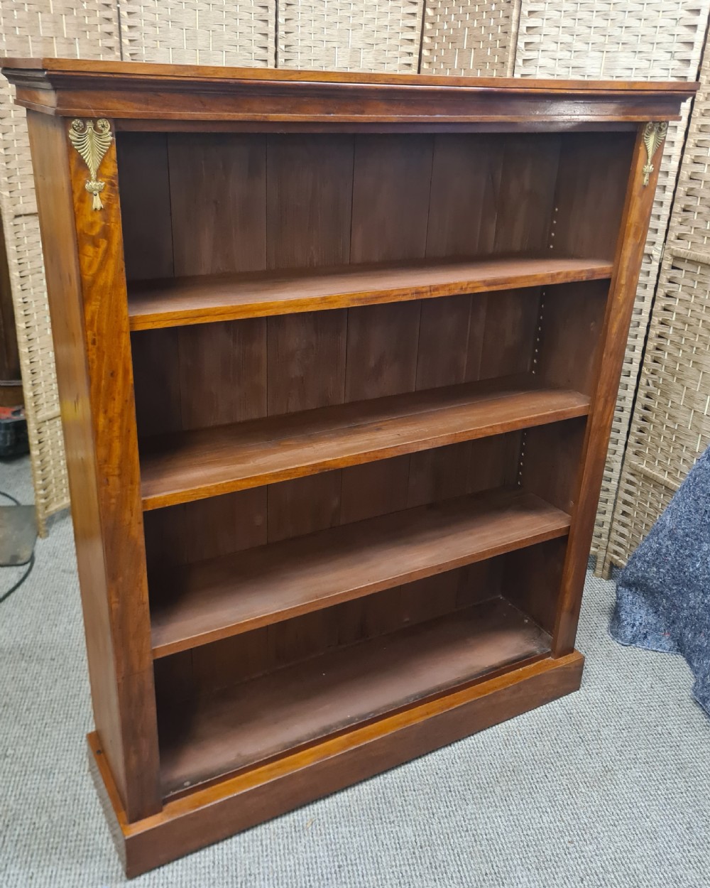 A nineteenth-century mahogany open bookcase featuring four tier shelves, a solid plinth base, and decorative brass mounts at the upper corners. View II