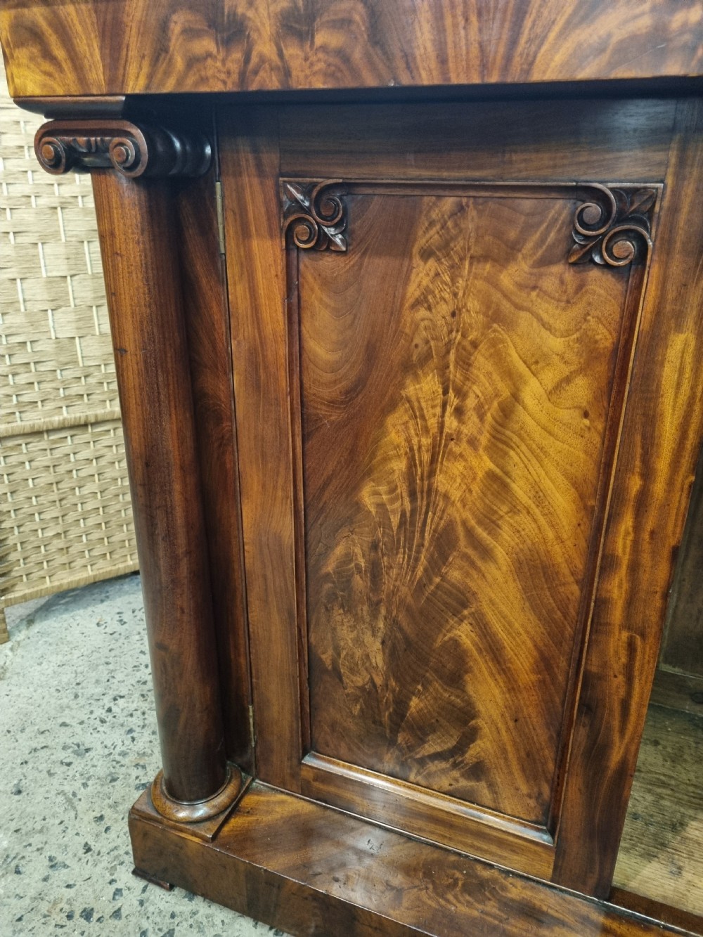An early nineteenth-century flame mahogany chiffonier featuring a carved cresting backboard with a single shelf over a two-door cabinet flanked by turned columns. View V