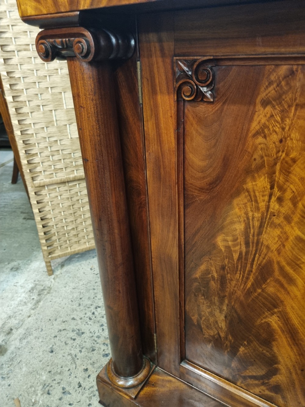An early nineteenth-century flame mahogany chiffonier featuring a carved cresting backboard with a single shelf over a two-door cabinet flanked by turned columns. View XI