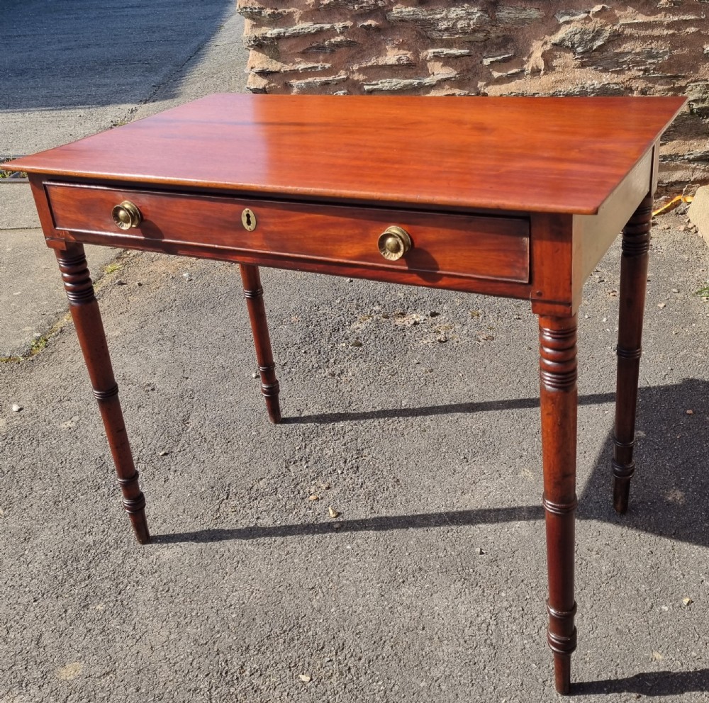 A Georgian mahogany writing table featuring a rectangular top, a single wide frieze drawer with brass ring handles, and four ring-turned legs.