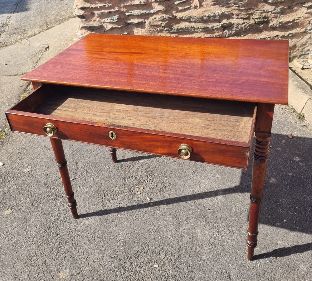 A Georgian mahogany writing table featuring a rectangular top, a single wide frieze drawer with brass ring handles, and four ring-turned legs. View IV