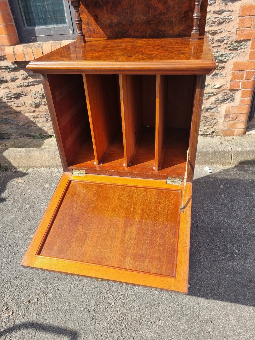 An Edwardian burr walnut music cabinet with a decorative scrolled upstand, a top shelf supported by turned pillars, a fall-front main compartment, and a lower single door cupboard. View VII