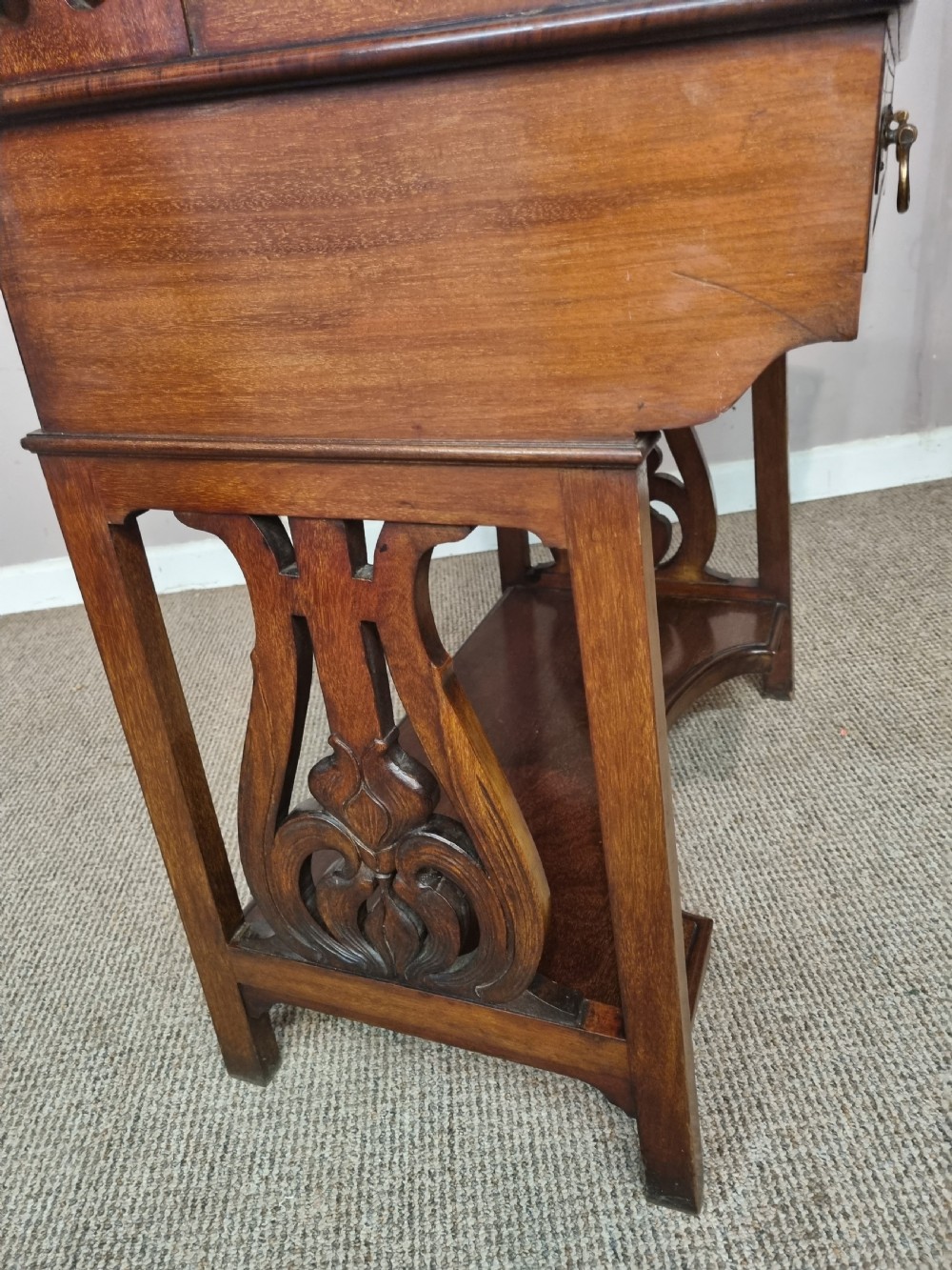 An Arts and Crafts mahogany bureau cabinet featuring a carved fall front slope, glazed upper cupboard doors, brass handles, and a lower shelf. View VIII