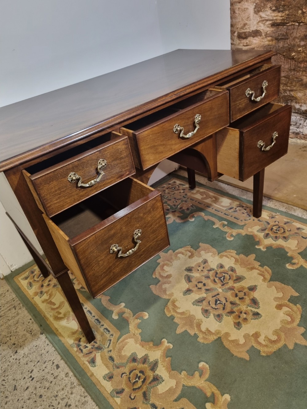A Georgian Revival mahogany kneehole dressing table featuring five drawers with ornate brass drop handles and an arched central apron. View III