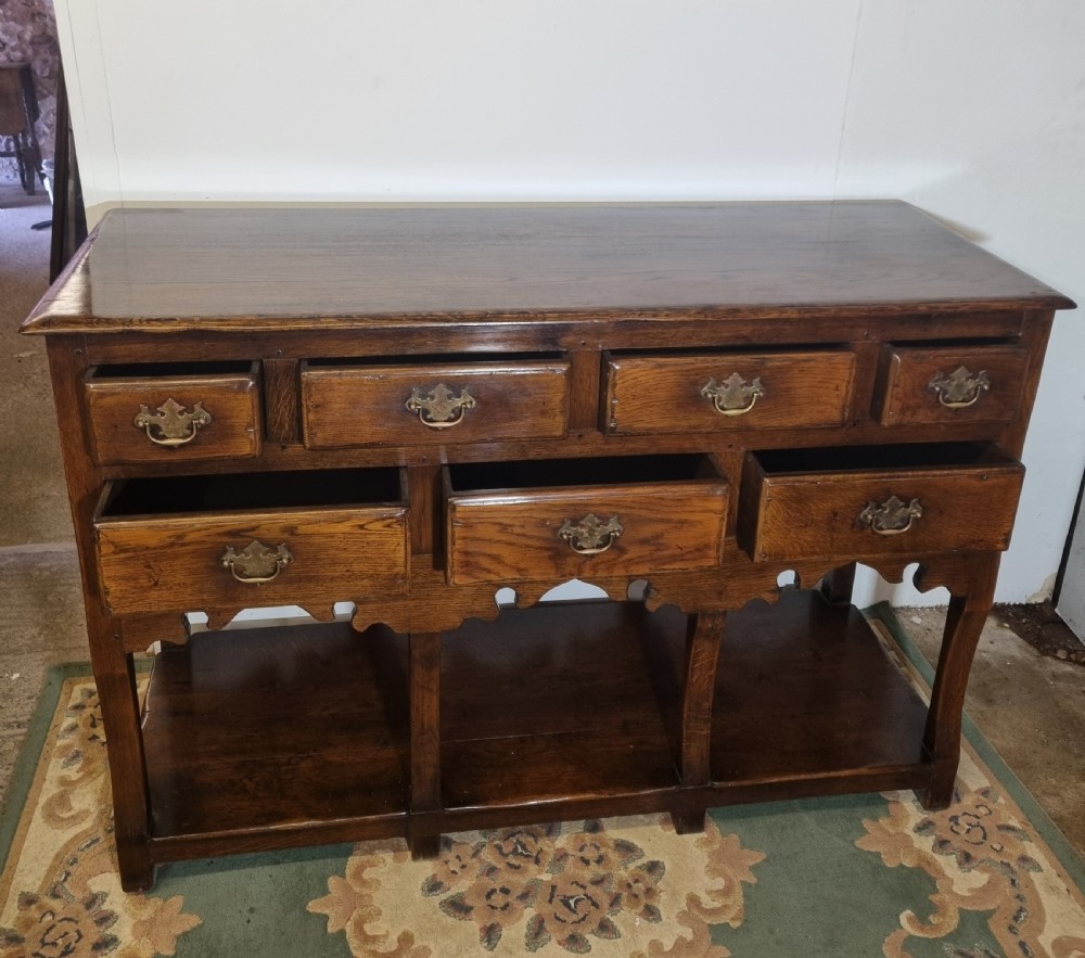 A dark oak Georgian-style dresser base featuring multiple drawers with brass handles, a scalloped apron, and an open lower potboard shelf. View II