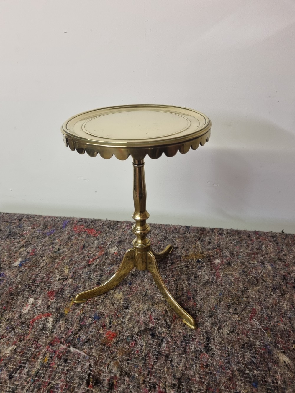 A Georgian cast brass kettle stand featuring a circular top with a scalloped rim, a turned baluster stem, and a tripod base.