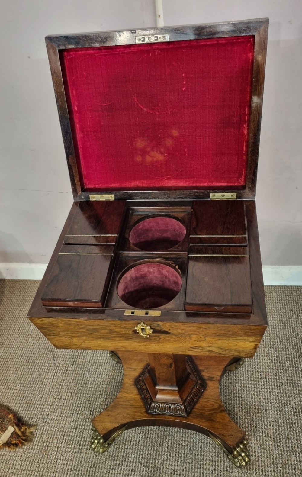 A Regency rosewood teapoy featuring a hinged sarcophagus chest supported by a tapered column and quadform base with brass lion paw feet. View II