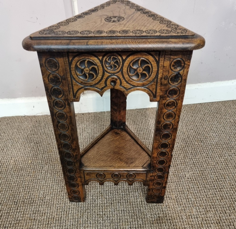 An early nineteenth-century dark carved oak triangular side table with a hinged top, lower shelf, and circular wheel carving details.