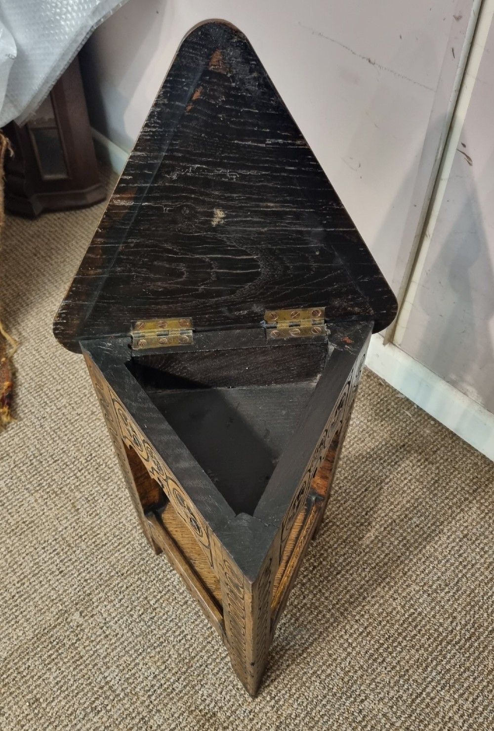 An early nineteenth-century dark carved oak triangular side table with a hinged top, lower shelf, and circular wheel carving details. View II