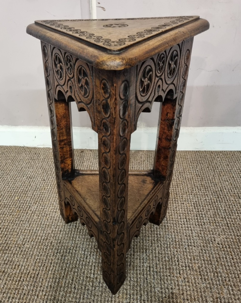 An early nineteenth-century dark carved oak triangular side table with a hinged top, lower shelf, and circular wheel carving details. View III