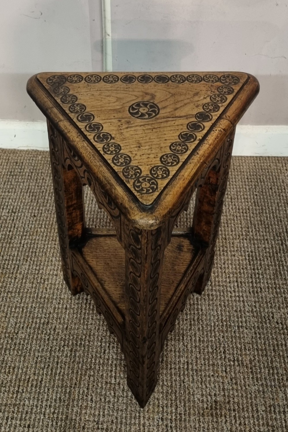 An early nineteenth-century dark carved oak triangular side table with a hinged top, lower shelf, and circular wheel carving details. View IV