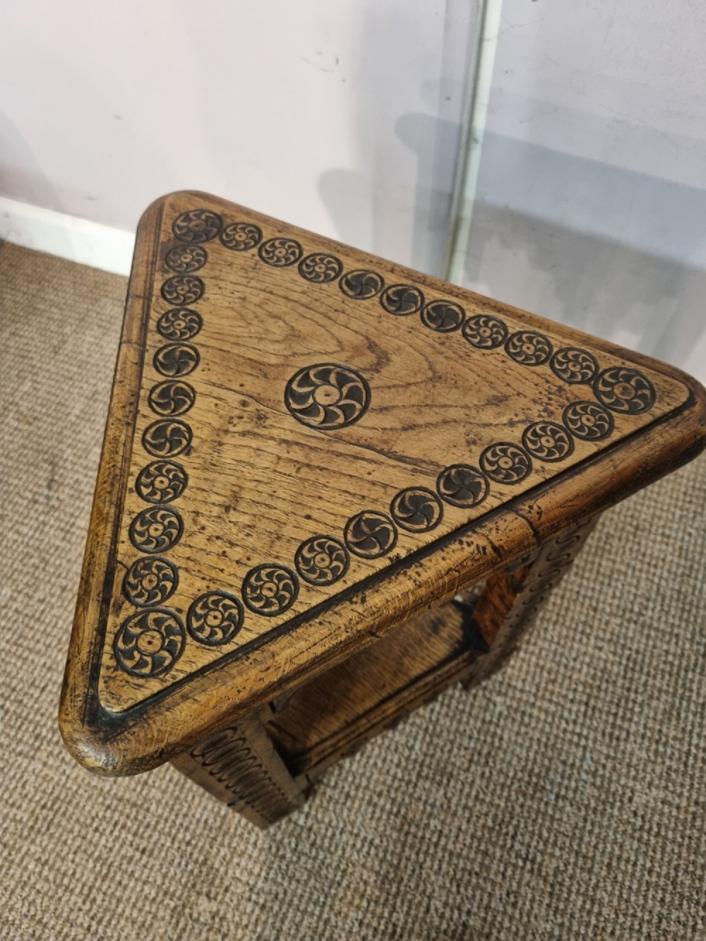 An early nineteenth-century dark carved oak triangular side table with a hinged top, lower shelf, and circular wheel carving details. View V