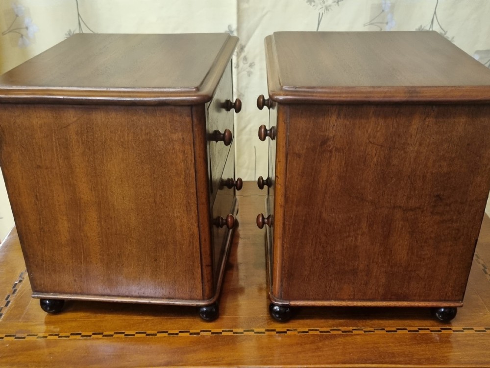 A matching pair of small Victorian mahogany tabletop chests, each featuring two drawers with turned wooden handles and resting on small dark bun feet. View V