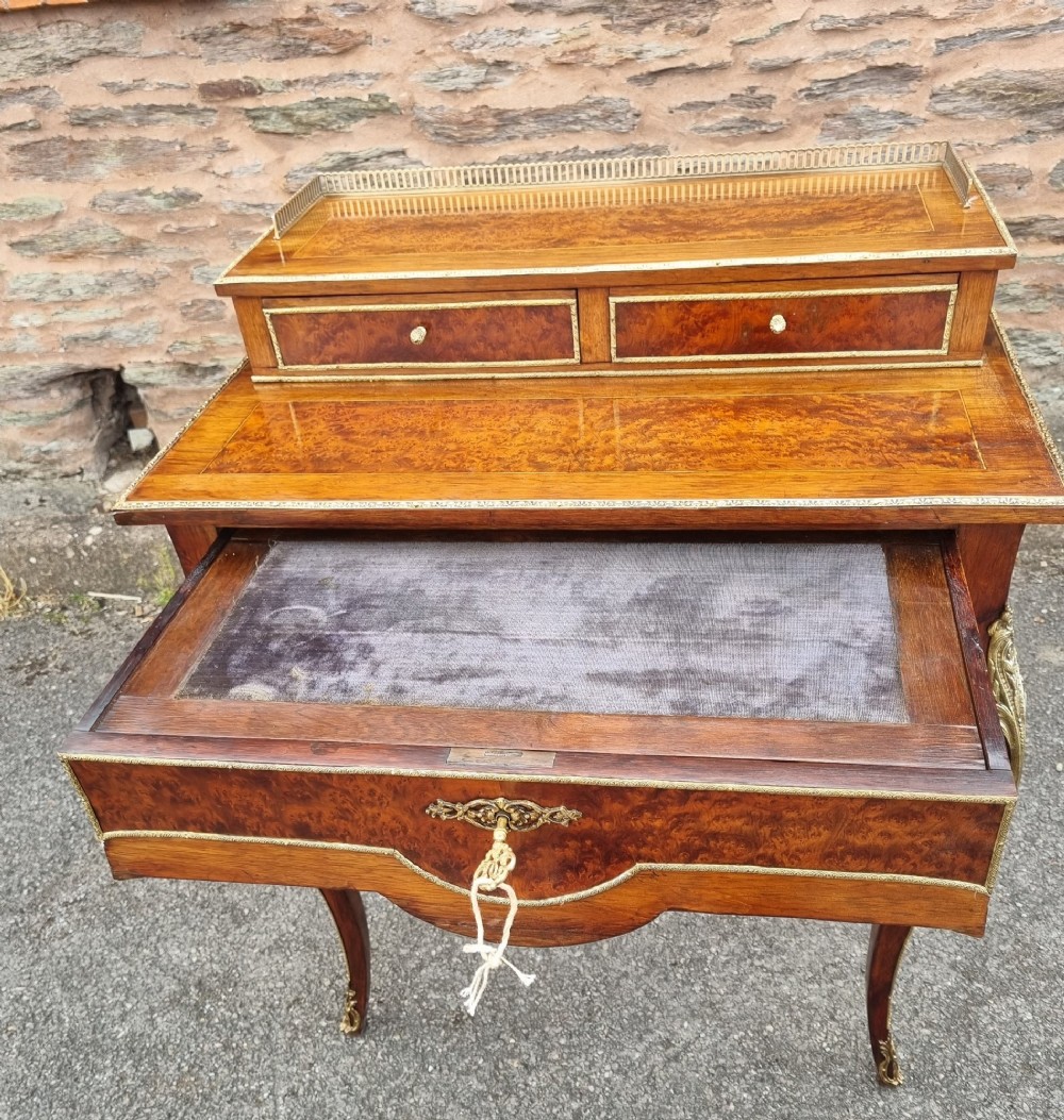 A nineteenth-century rosewood and amboyna veneer bonheur du jour desk featuring cabriole legs, gilt-metal mounts, and a brass gallery rail on the raised upper shelf. View V