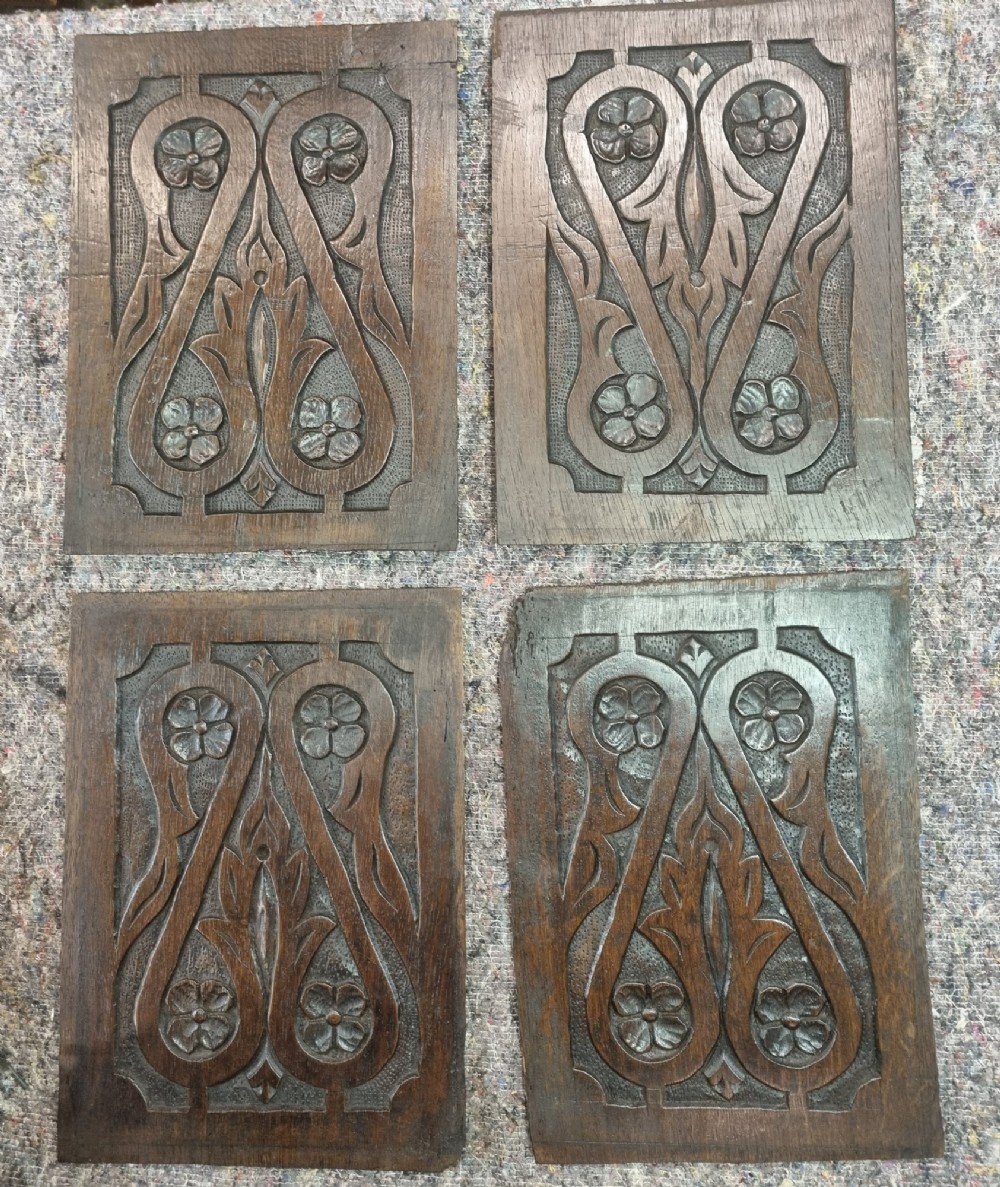 A set of four dark oak carved wooden panels featuring relief floral and foliate motifs with textured stippled backgrounds.