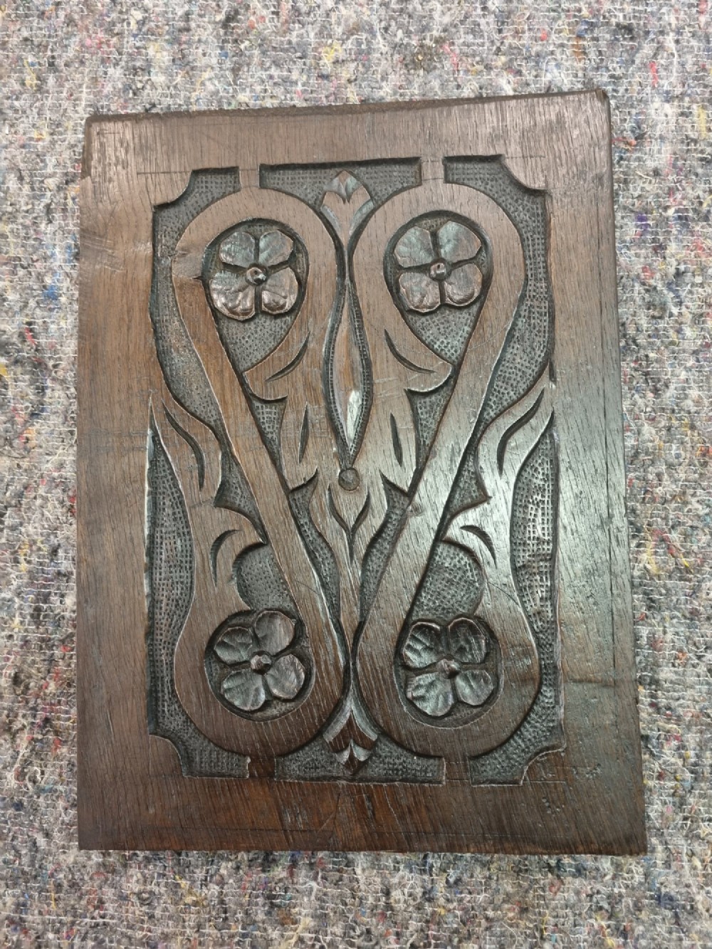 A set of four dark oak carved wooden panels featuring relief floral and foliate motifs with textured stippled backgrounds. View V