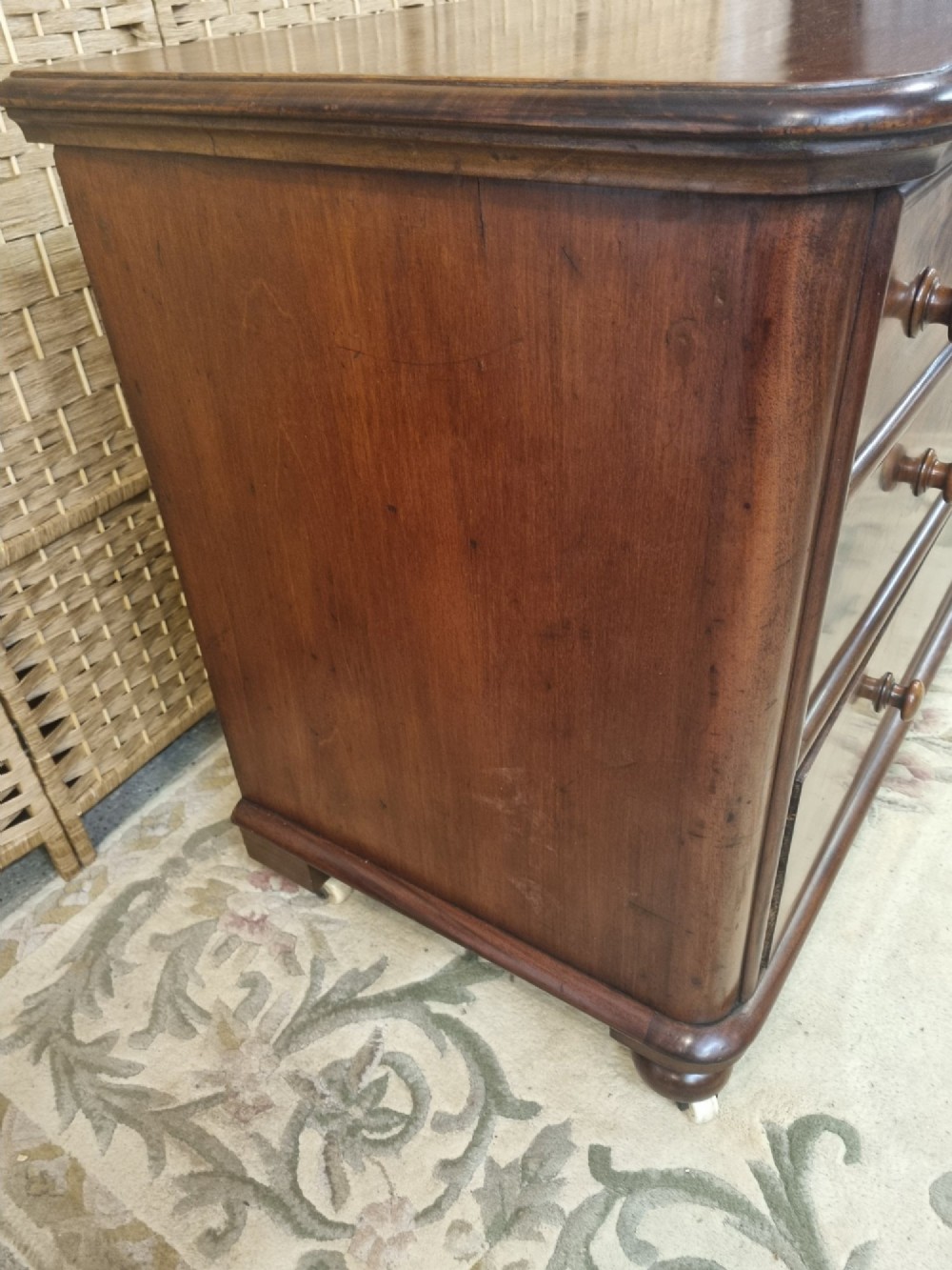 A nineteenth-century flame mahogany chest of drawers featuring two short over two long drawers with turned wooden knobs, rounded moulding, and short turned feet with castors. View V