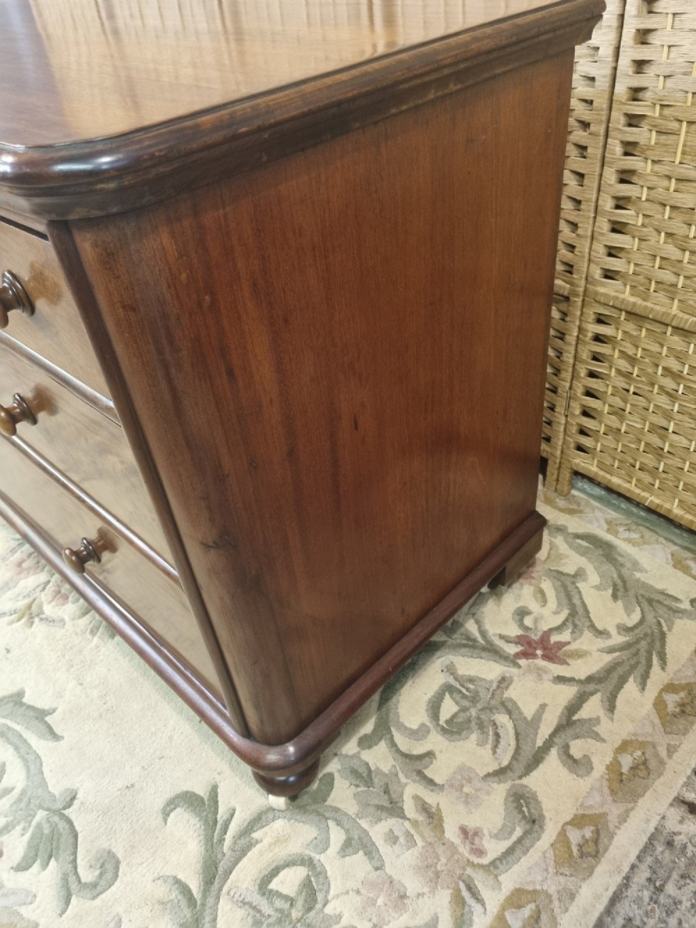 A nineteenth-century flame mahogany chest of drawers featuring two short over two long drawers with turned wooden knobs, rounded moulding, and short turned feet with castors. View VI