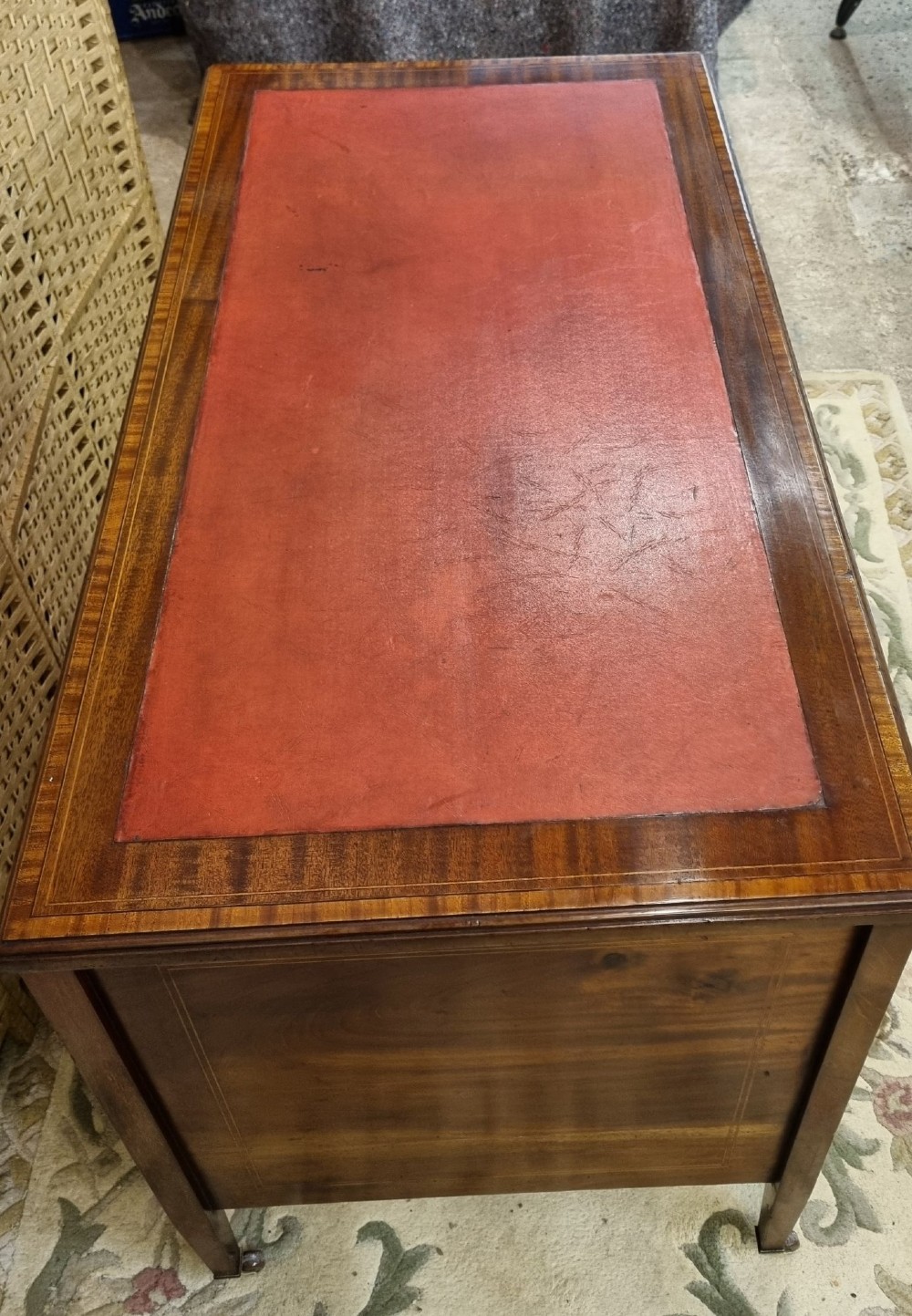 An Edwardian mahogany writing desk featuring nine inlaid drawers, a terracotta leather writing surface, brass knob handles, and tapered legs on castors. View III