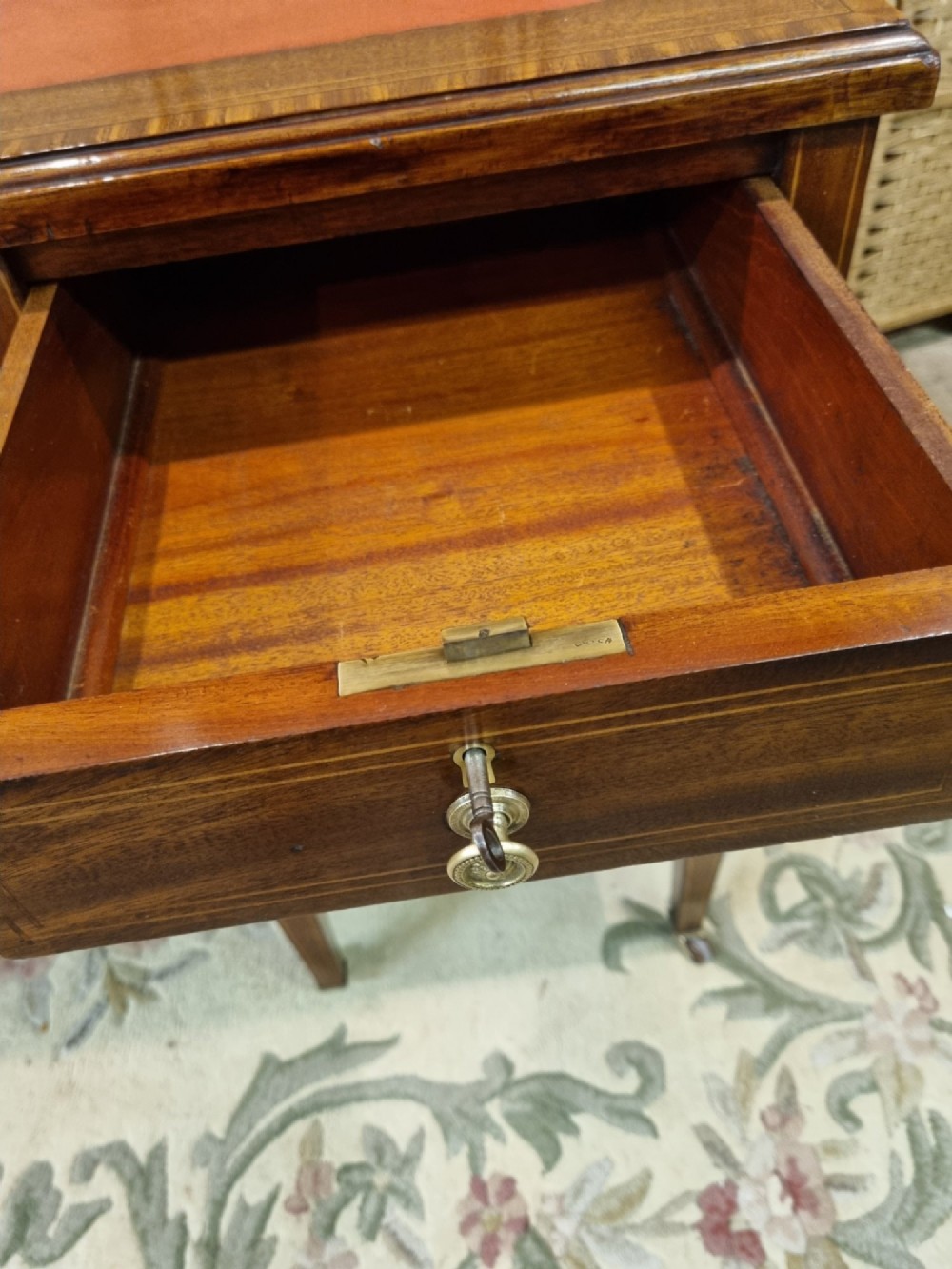 An Edwardian mahogany writing desk featuring nine inlaid drawers, a terracotta leather writing surface, brass knob handles, and tapered legs on castors. View VII