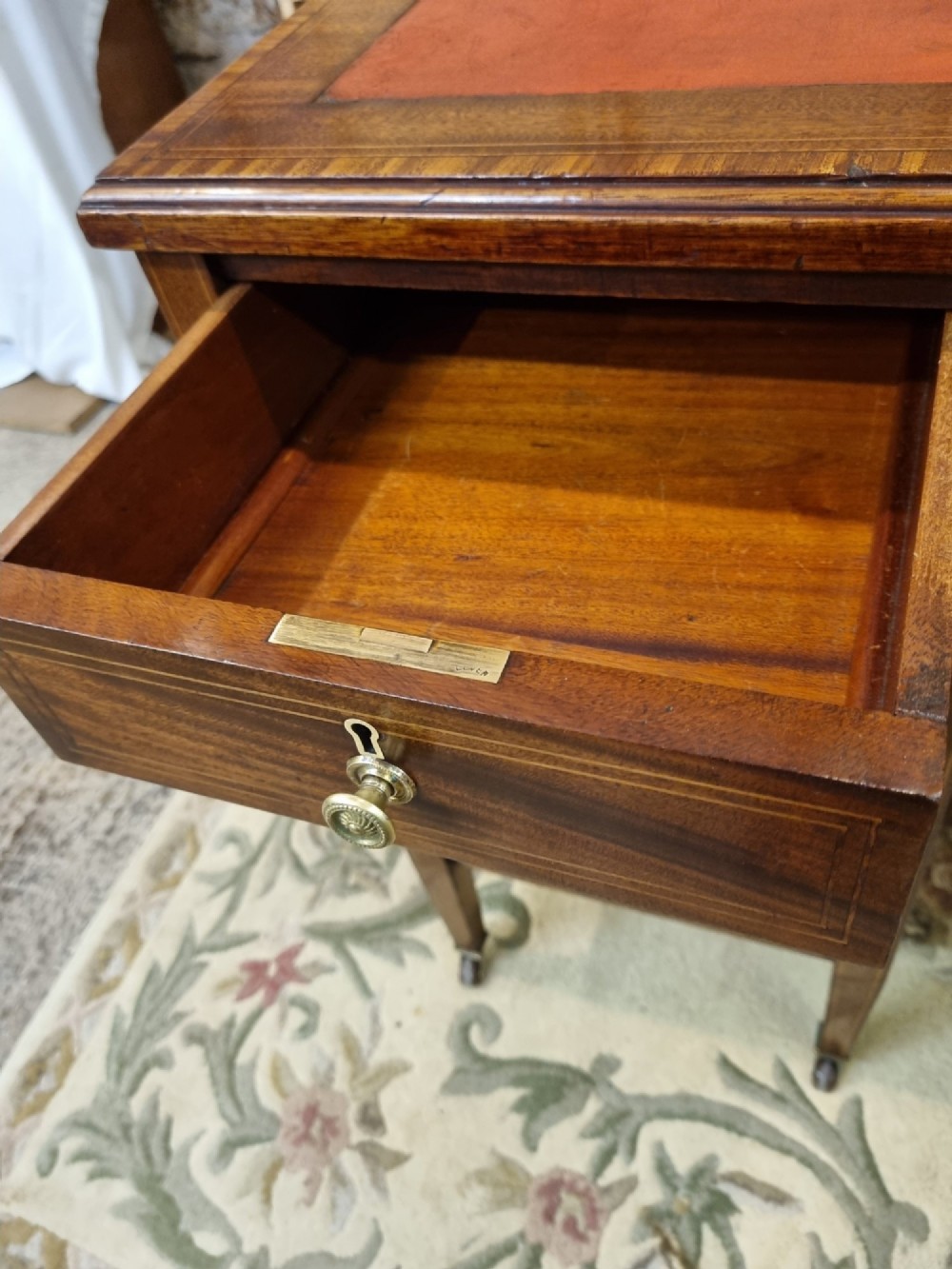 An Edwardian mahogany writing desk featuring nine inlaid drawers, a terracotta leather writing surface, brass knob handles, and tapered legs on castors. View VIII