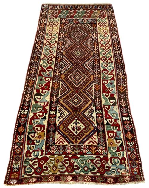 fig 1. A hand-knotted antique Caucasian wool runner rug featuring a central column of diamond medallions framed by intricate geometric borders in terracotta red, cream, and green.