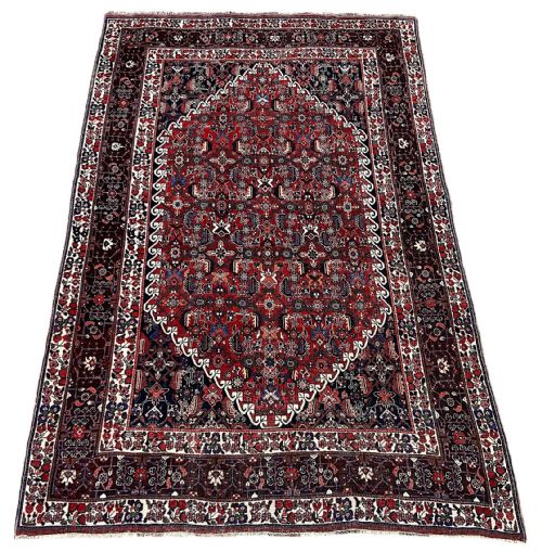 fig 1. An antique hand-knotted Qashqai rug with a central stepped medallion in red and navy blue surrounded by geometric tribal motifs and patterned borders.