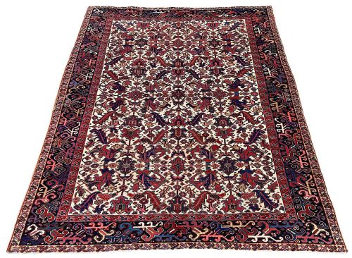 fig 1. An antique hand-knotted Heriz carpet featuring an ivory central field filled with red and navy geometric floral motifs and framed by a dark blue patterned border.
