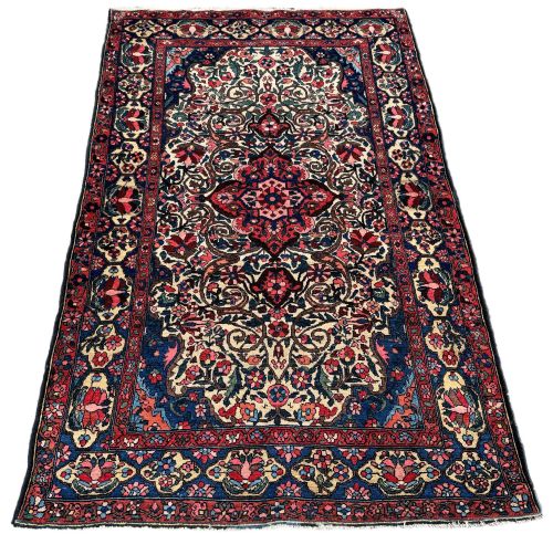 fig 1. An antique hand-knotted Bakhtiar wool area rug featuring a central starburst medallion surrounded by intricate floral scrolling patterns in navy blue, red, cream, and green shades with a multi-layered border.