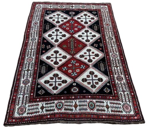 fig 1. An antique Lori wool carpet featuring repeating diamond motifs in red and cream against a dark navy background surrounded by geometric borders.