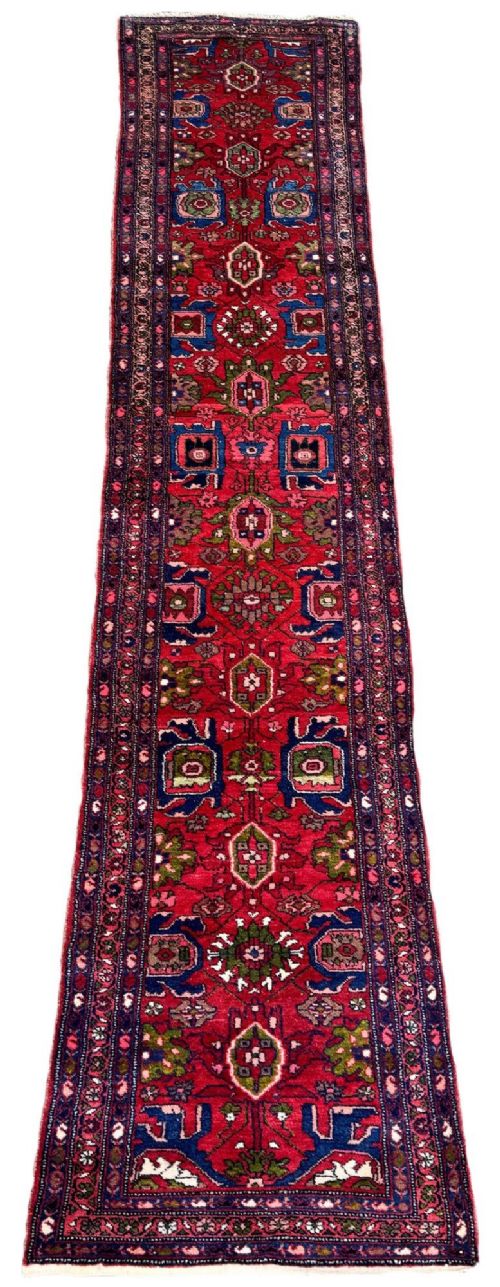 fig 1. A long hand-knotted Persian Hamadan runner rug featuring a crimson red field decorated with repeated geometric medallions and dark blue patterned borders.
