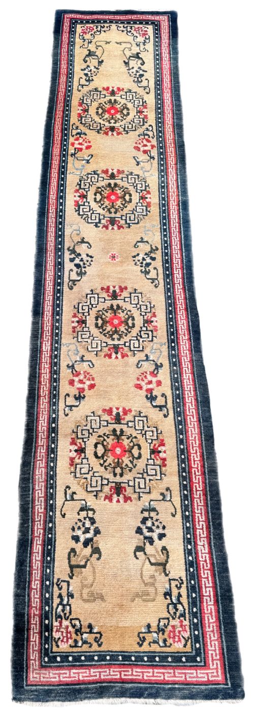 fig 1. A long antique Tibetan wool runner rug featuring four circular geometric medallions on a beige field bordered by red key-fret patterns and indigo blue edges.
