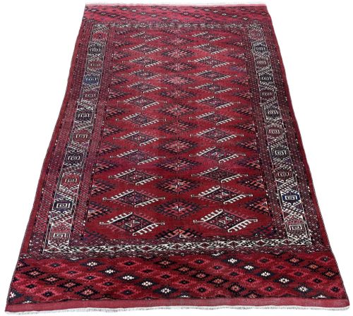fig 1. An antique hand-knotted Turkmen Yomut wool carpet featuring repeating geometric diamond motifs across a deep red field with framed borders.