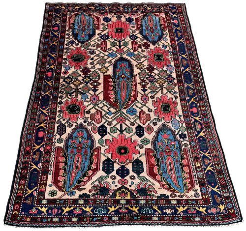 fig 1. An antique Persian Bakhtiar wool rug featuring intricate geometric floral patterns and bird motifs in blue, pink, and red set against a cream background with a dark blue decorative border.