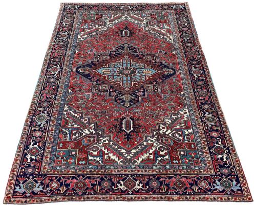 fig 1. A large hand-knotted antique Heriz wool carpet featuring a prominent central geometric medallion on a deep red field framed by dark navy and cream borders.