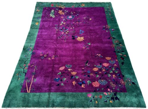 fig 1. A large hand-knotted wool carpet featuring a vibrant magenta central field framed by a rich jade green border with asymmetrical floral and bamboo motifs.