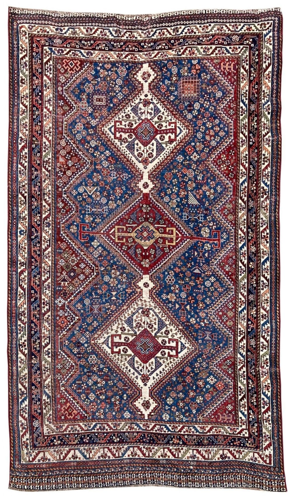 An antique Persian Qashqai wool rug displaying three diamond medallions on a navy blue field filled with geometric tribal motifs and framed by a detailed multi-tiered border.