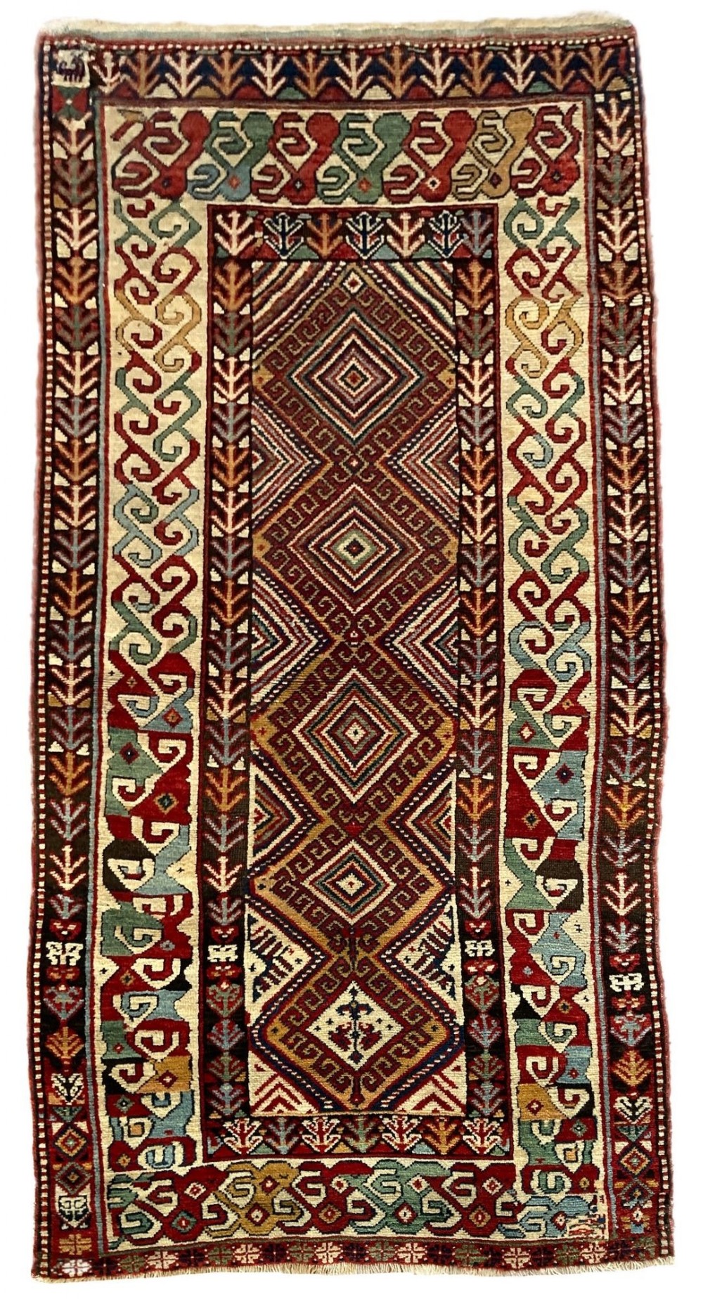 A hand-knotted antique Caucasian wool runner rug featuring a central column of diamond medallions framed by intricate geometric borders in terracotta red, cream, and green.