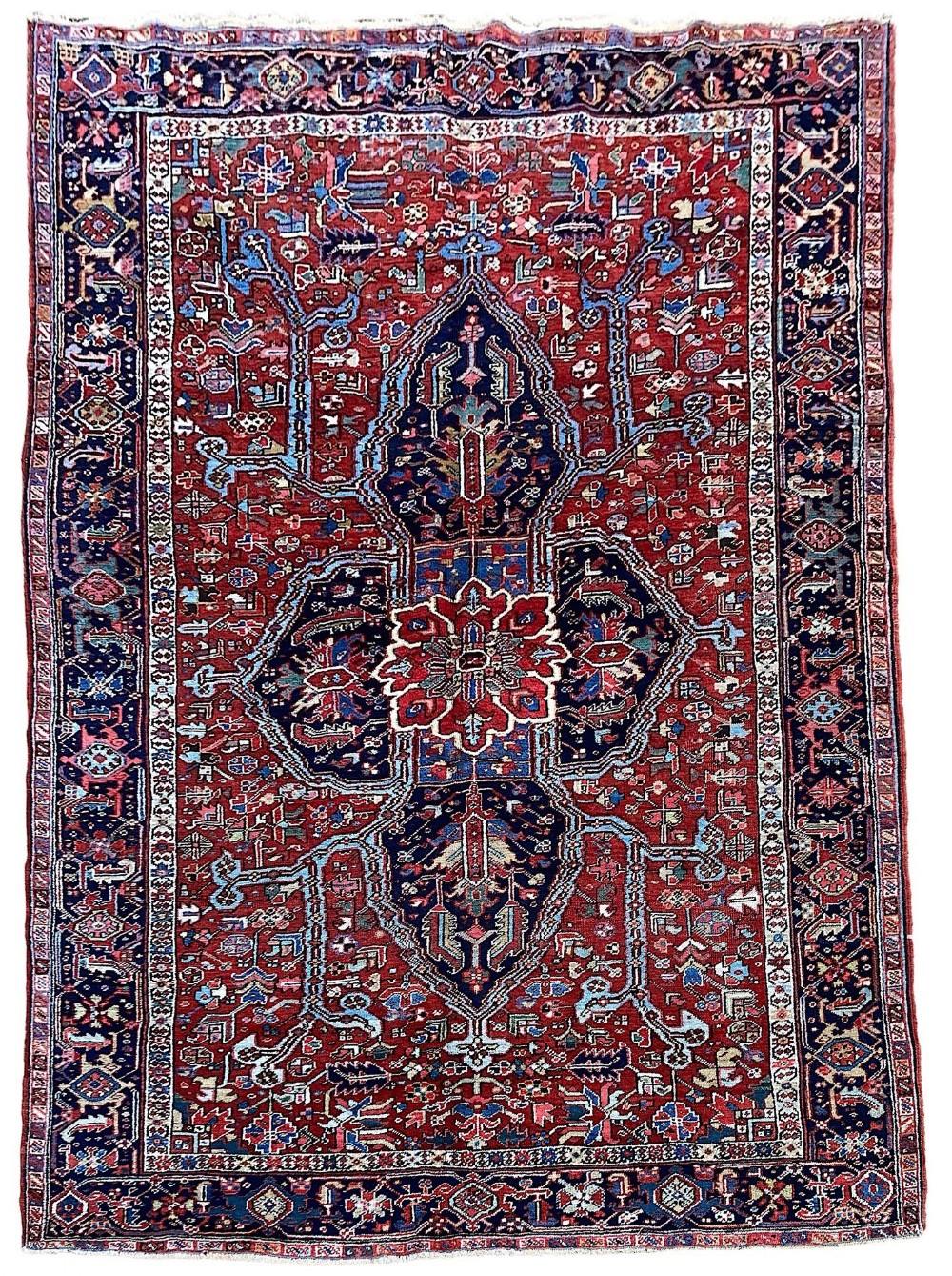 An antique hand-knotted Heriz wool carpet with a large geometric central medallion on a terracotta red field surrounded by navy blue borders.