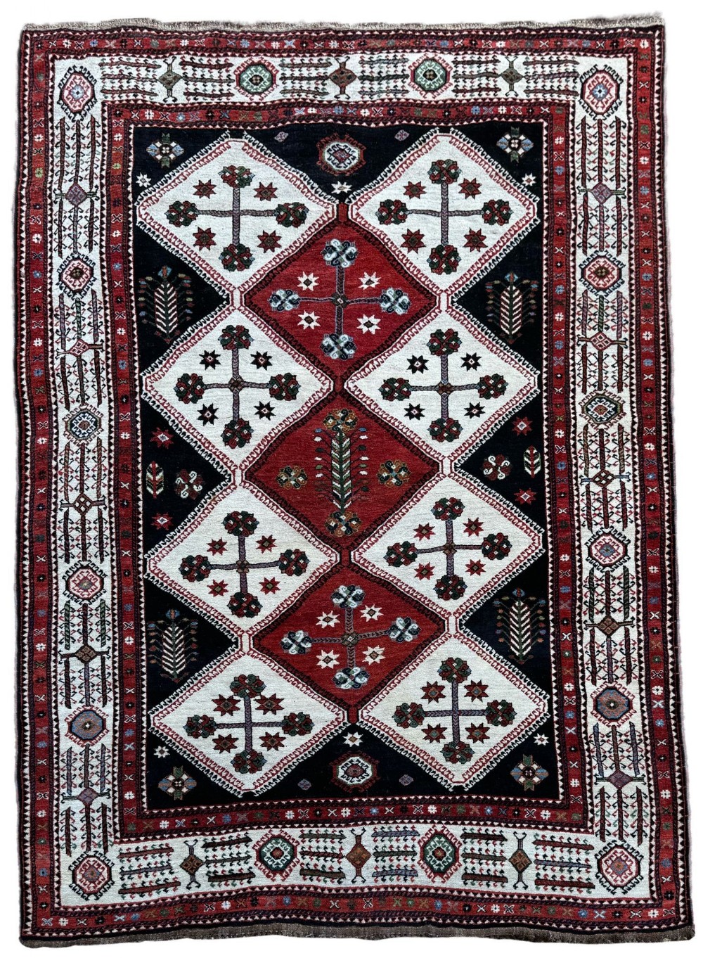 An antique Lori wool carpet featuring repeating diamond motifs in red and cream against a dark navy background surrounded by geometric borders.
