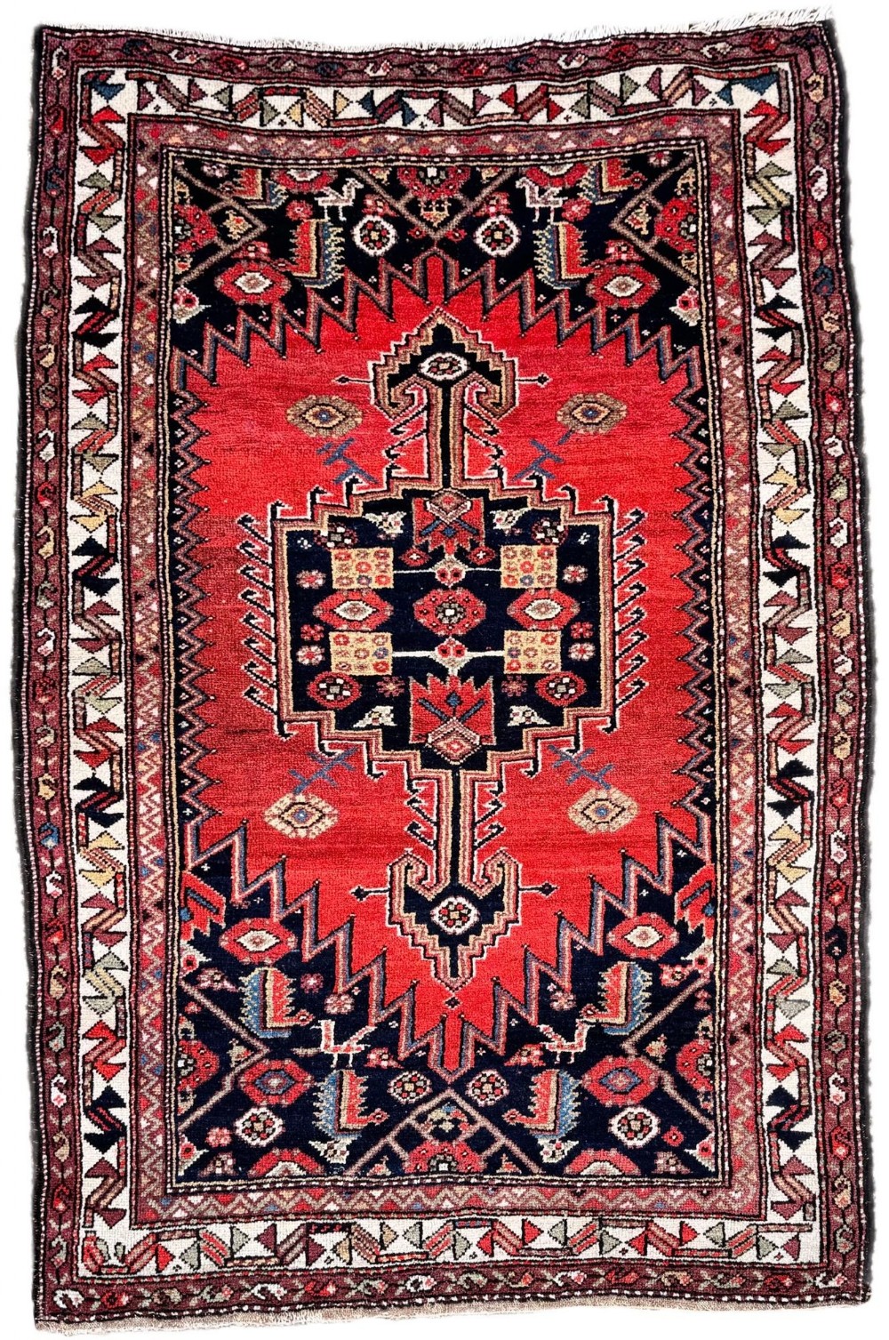 Hand-knotted antique Luri wool rug featuring a dark central stepped medallion on a crimson field enclosed by geometric borders.
