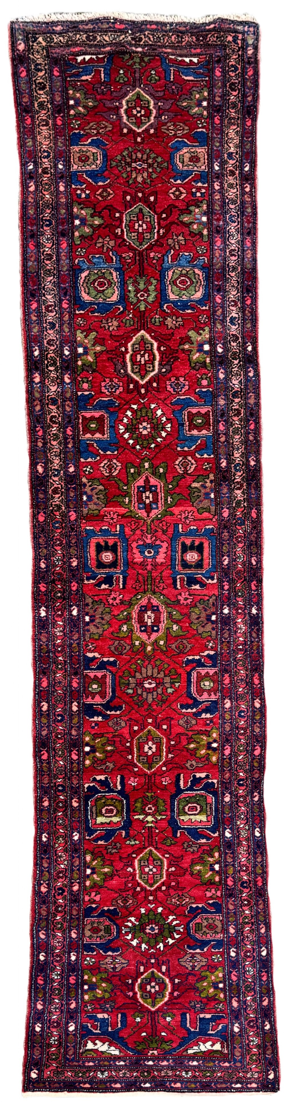 A long hand-knotted Persian Hamadan runner rug featuring a crimson red field decorated with repeated geometric medallions and dark blue patterned borders.