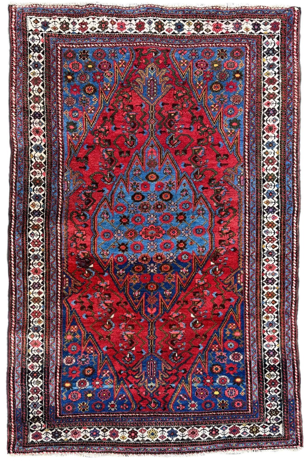 An antique hand-knotted Persian Hamadan wool rug featuring a blue stepped central medallion surrounded by a red geometric field and decorated ivory borders.