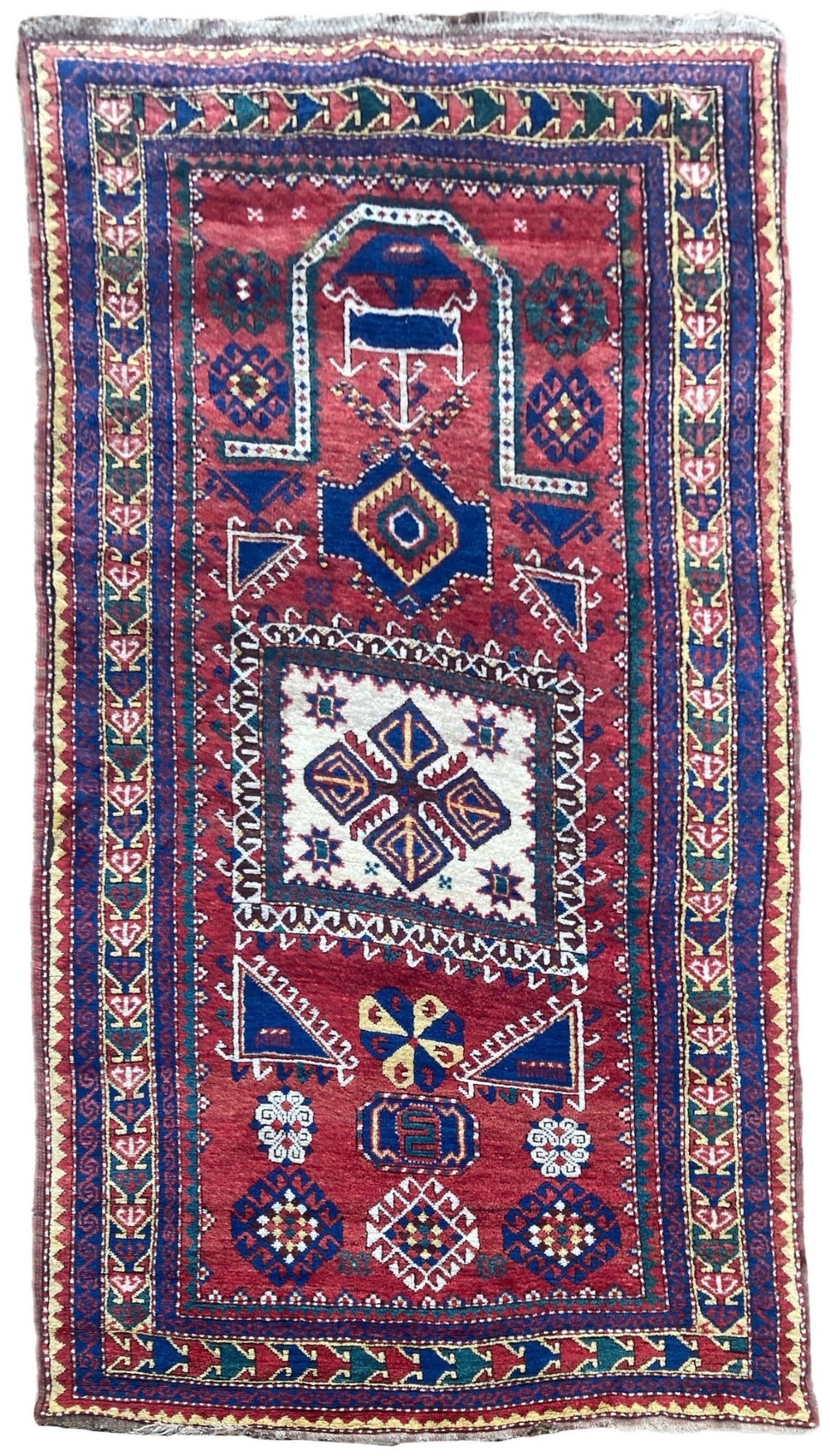 A hand-knotted Caucasian prayer rug featuring a red central field with a pointed mihrab niche, geometric medallions, and multi-band patterned borders in navy blue, red, and cream.