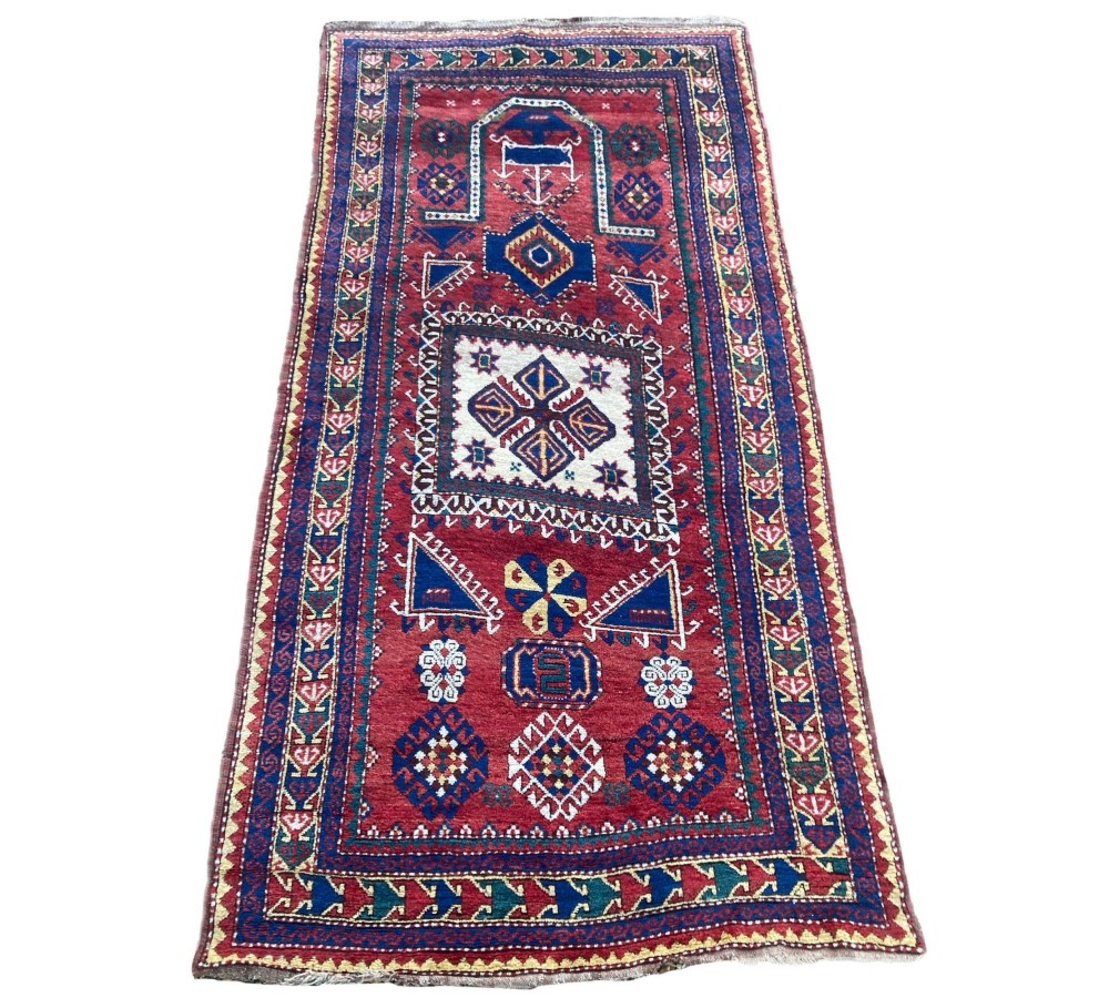 A hand-knotted Caucasian prayer rug featuring a red central field with a pointed mihrab niche, geometric medallions, and multi-band patterned borders in navy blue, red, and cream. View II