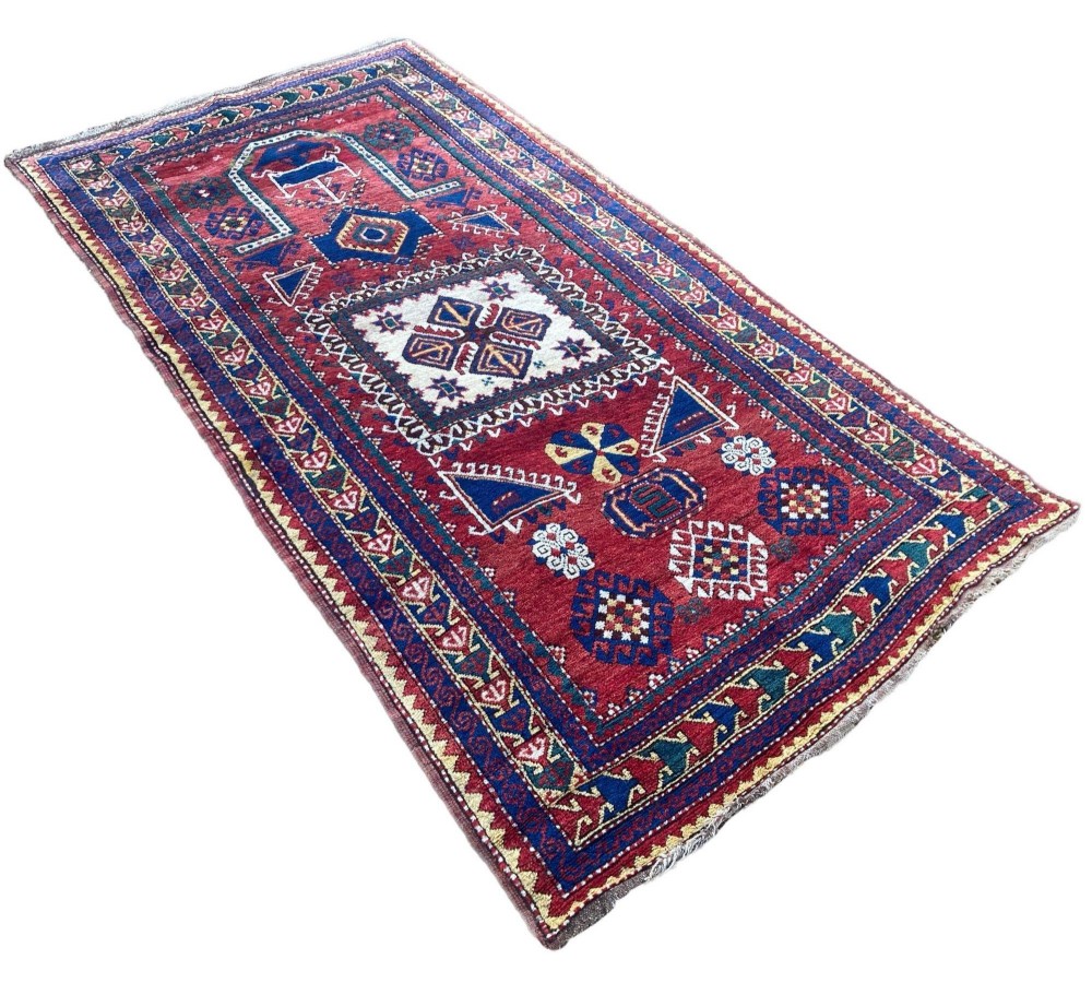 A hand-knotted Caucasian prayer rug featuring a red central field with a pointed mihrab niche, geometric medallions, and multi-band patterned borders in navy blue, red, and cream. View III